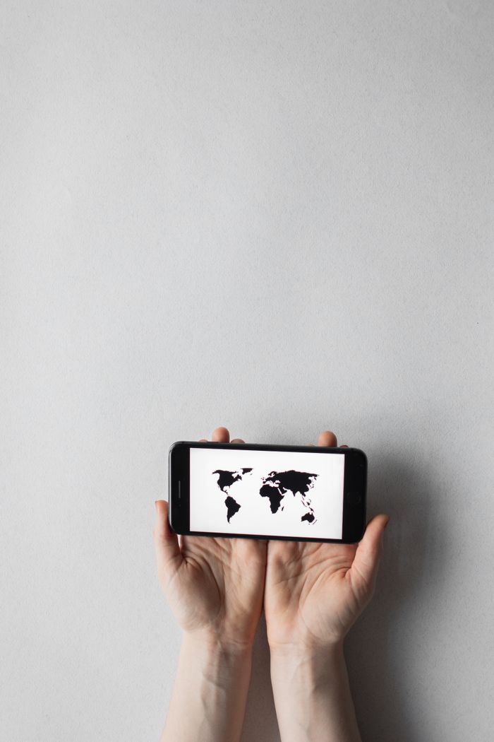 Hands holding a smartphone displaying a world map on a white background, emphasizing global connectivity.